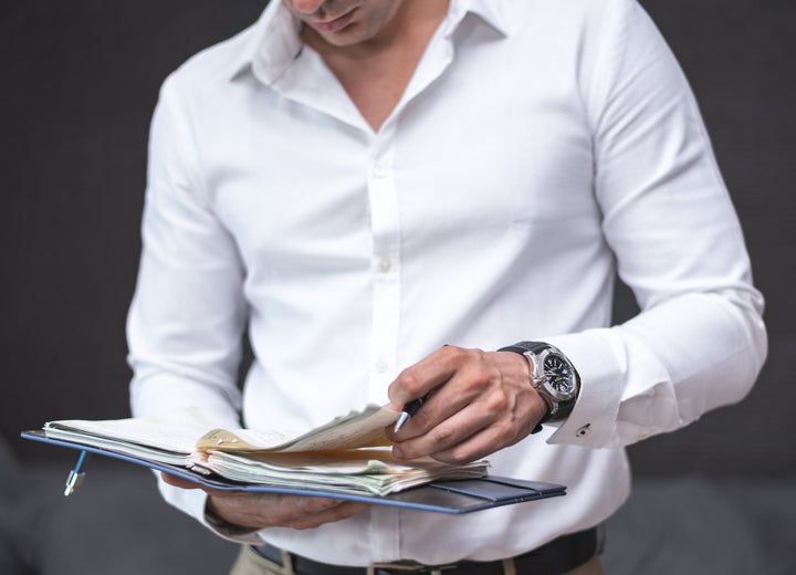 man in business clothes wearing a swiss watch and reading from a binder.